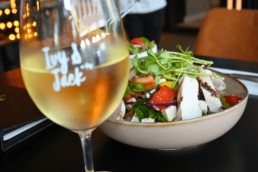 Wine Glass containing white wine with a salad blurred in the backgorund